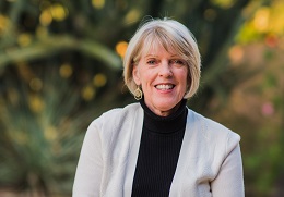 Smiling woman outdoors with blurred foliage background.