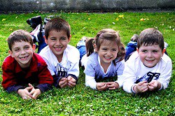 Four children lying on grass, smiling together.