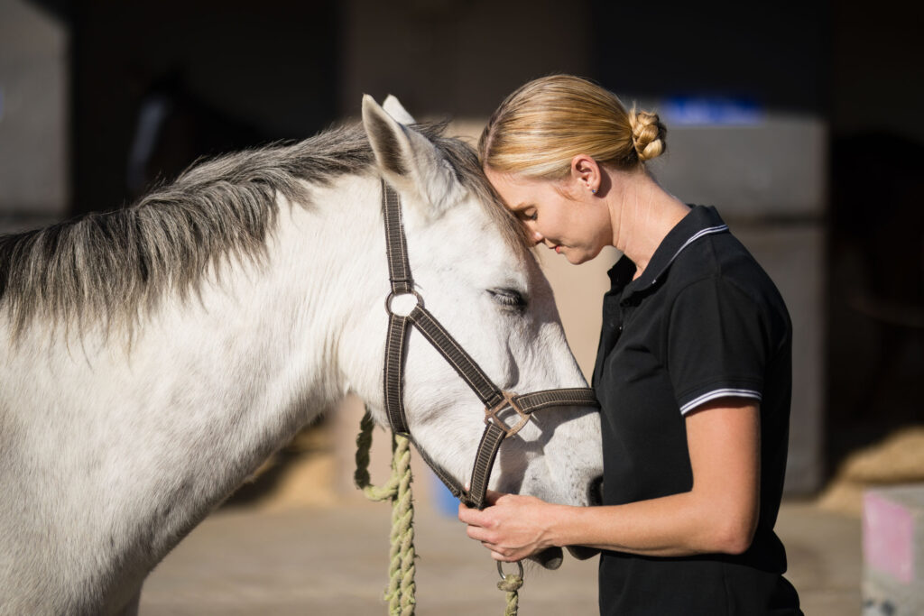 Woman bonding with a white horse tenderly.